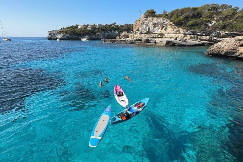 A clear blue sea with boats, a rocky coastline, and buildings on a hill. 3