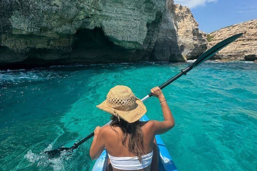 A person kayaking in clear turquoise water with rocky cliffs in the background. 1