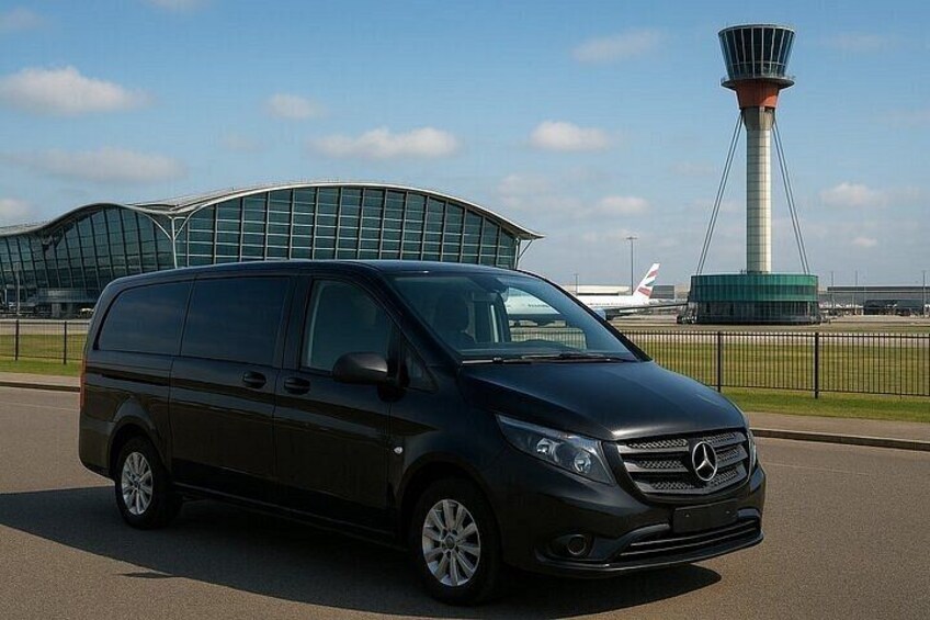 A black Mercedes-Benz minivan parked on a road with a modern airport terminal and a control tower in the background. 3