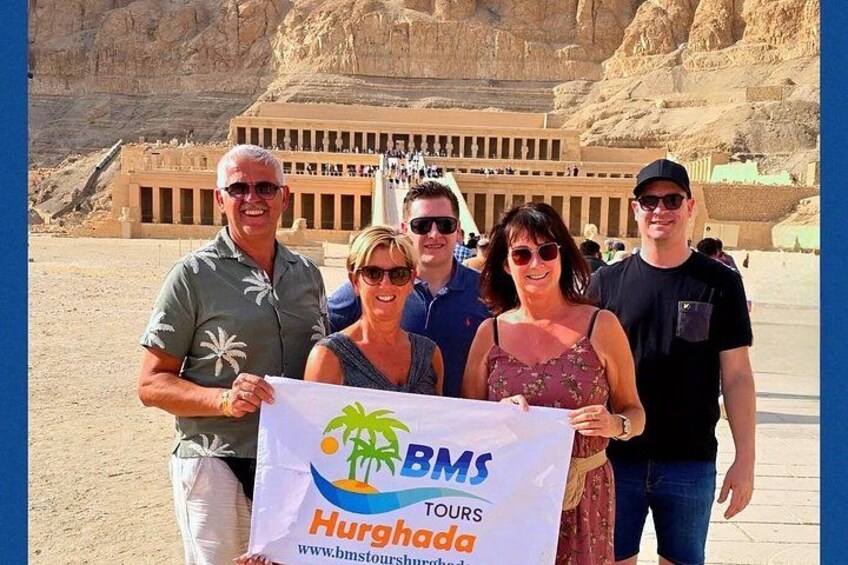 A group of people holding a banner with 'BMS Tours' and 'Hurghada' written on it, standing in front of a large ancient structure. 5