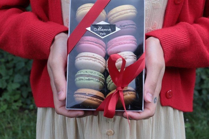 Une personne tenant une boîte de macarons, ornée d’un ruban rouge. 3