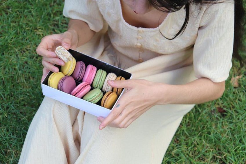 Une personne tenant une boîte de macarons multicolores à l’extérieur. 2