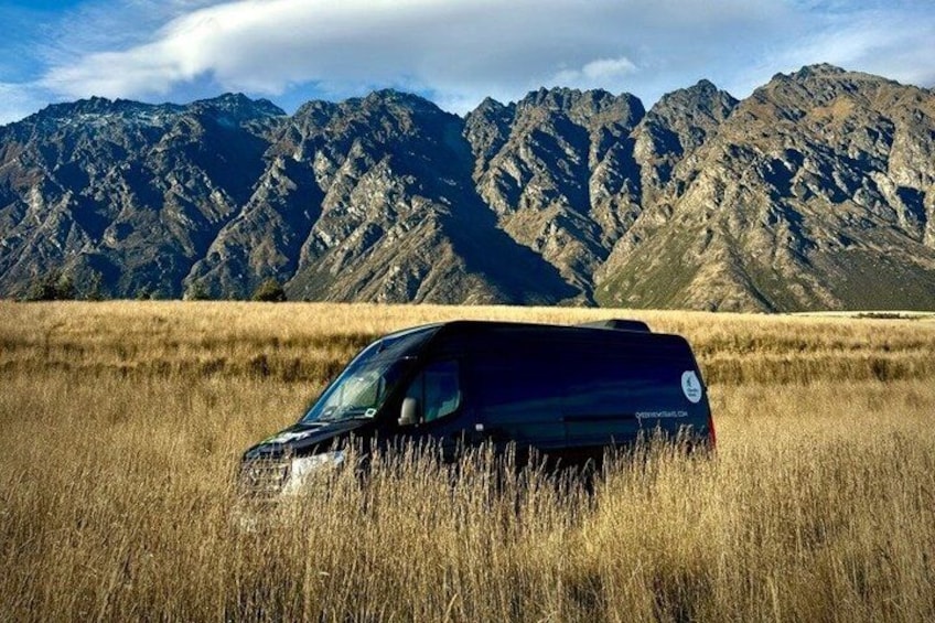 A black van parked in a field with mountains in the background. 3