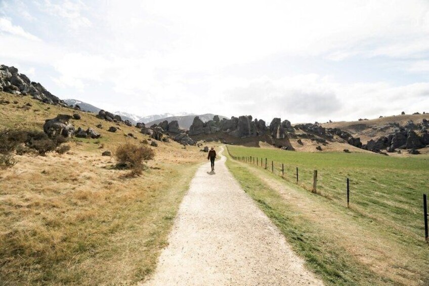 A gravel path flanked by grass and rocks, leading towards a rocky hill. 4