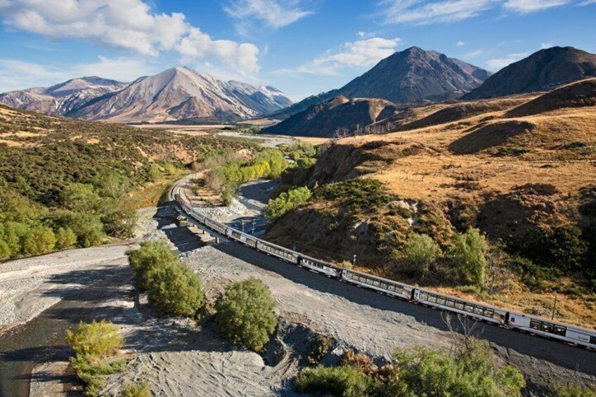 A train traveling through a mountainous landscape with a river and sparse vegetation. 5