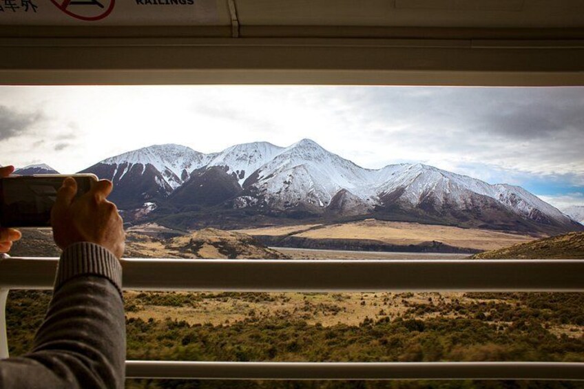 A person taking a photo of snow-capped mountains through a train window. 2