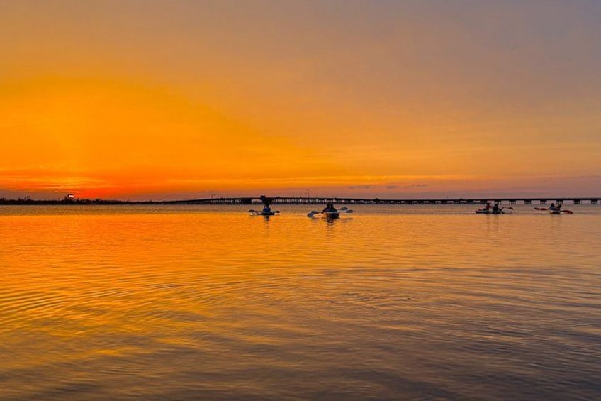 Un atardecer sobre un cuerpo de agua tranquilo con un puente a lo lejos. 4