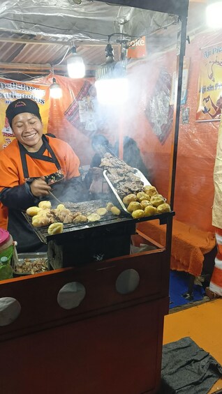 A street food vendor grilling meat and potatoes. 1