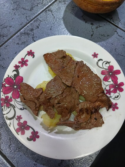 A plate of cooked beef and potatoes on a tiled surface. 5