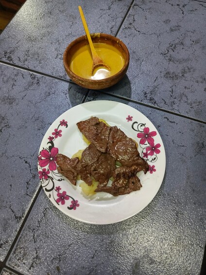 A plate of cooked meat with a yellow sauce and a wooden bowl with a spoon on a textured table. 3