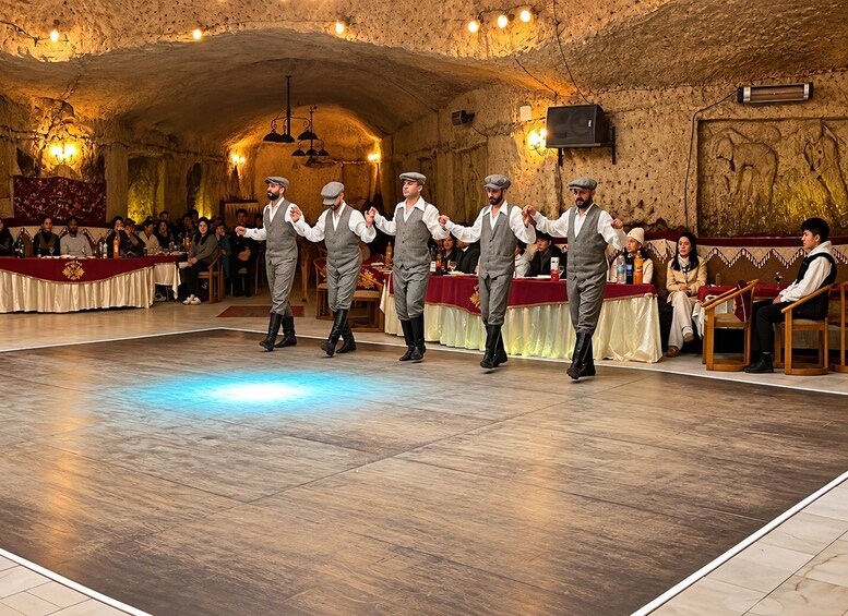 A group of men in grey suits performing a dance in a hall with a wooden floor and stone walls. 5