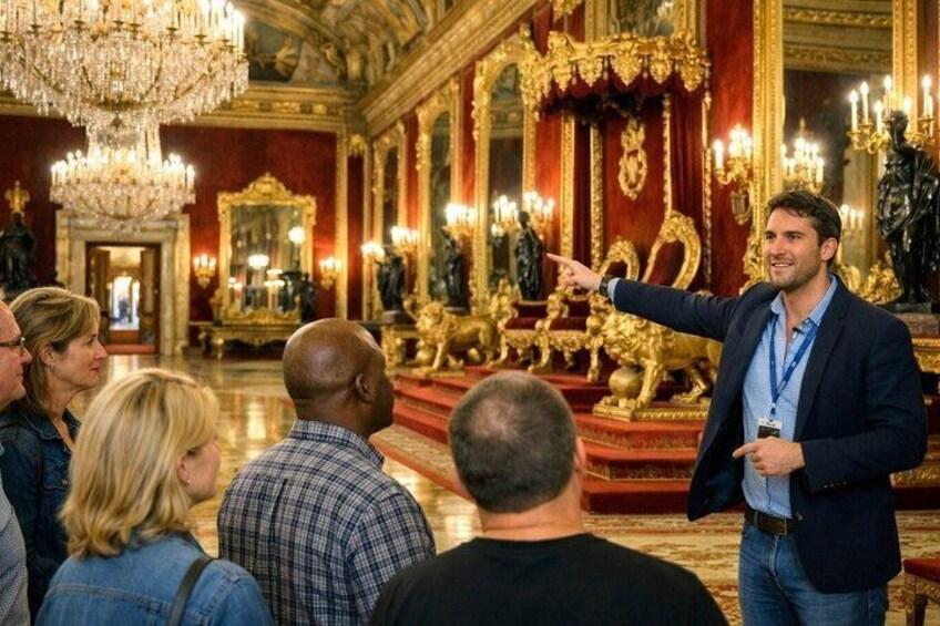 Un hombre señala una estatua dorada en un salón espacioso con decoraciones elaboradas y candelabros. 1