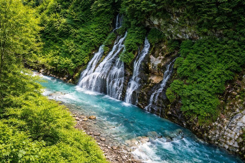 A turquoise river flowing through a forested gorge with multiple waterfalls. 2