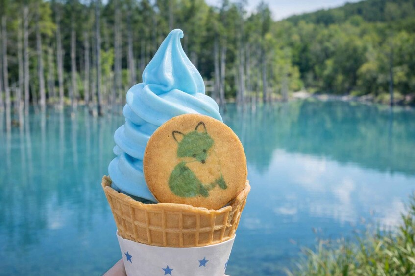 A waffle cone with a blue swirl of ice cream and a cookie with a green bear design, set against a lake and forest backdrop. 4