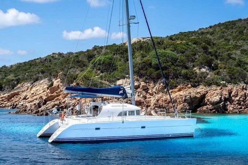 A white yacht on turquoise water with a rocky coastline and greenery in the background. 3