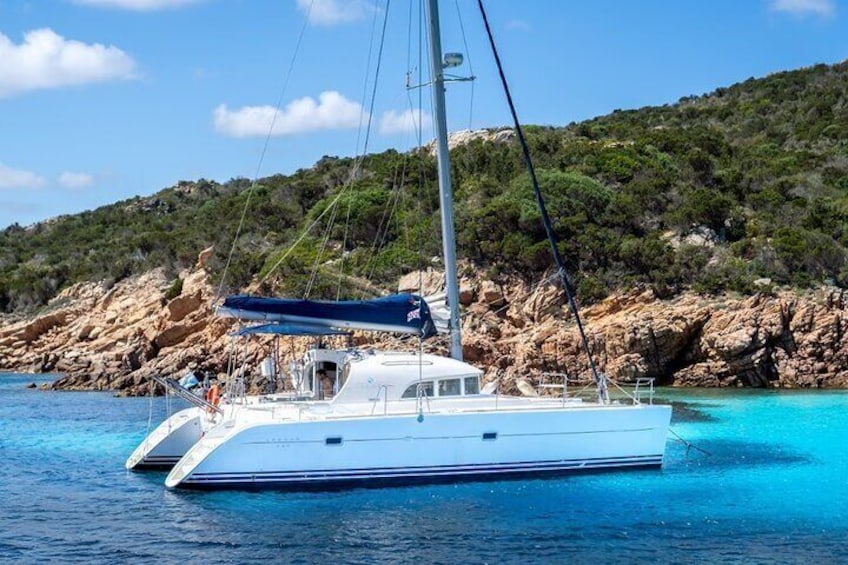 A white yacht with a blue canopy on calm turquoise waters, surrounded by rocky cliffs and greenery. 3