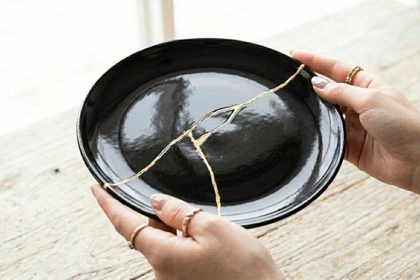 En person holder en sort tallerken med gylden snor. 3