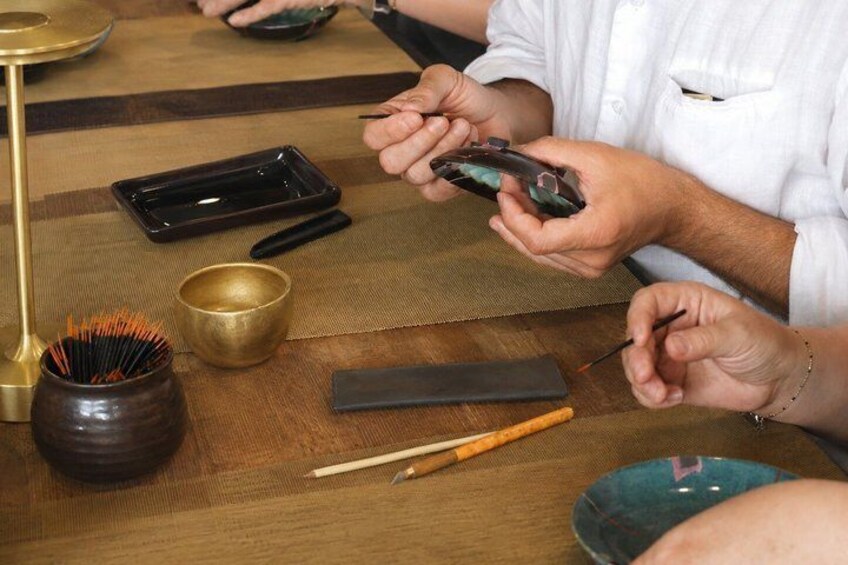 A person holding a smartphone, a black rectangular object, and a brush on a wooden table with a mat. 5