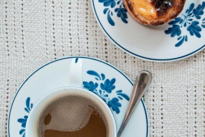 En kopp kaffe på ett litet fat med en sked, och en tallrik med ett bakverk. 2