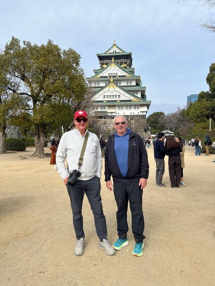 Two people standing in front of a castle with a green roof and gold accents. 5