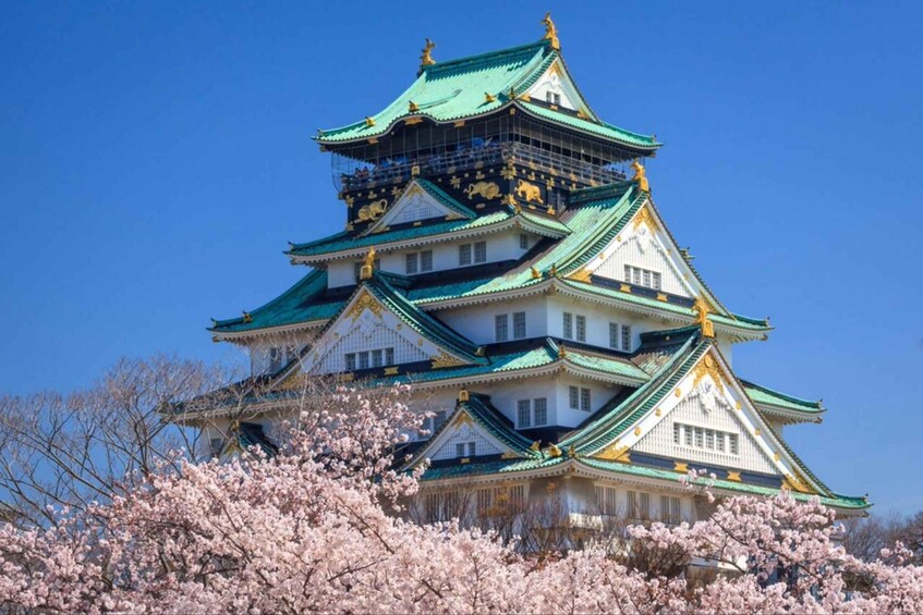 A multi-tiered castle with green and white roofs, surrounded by cherry blossoms. 1