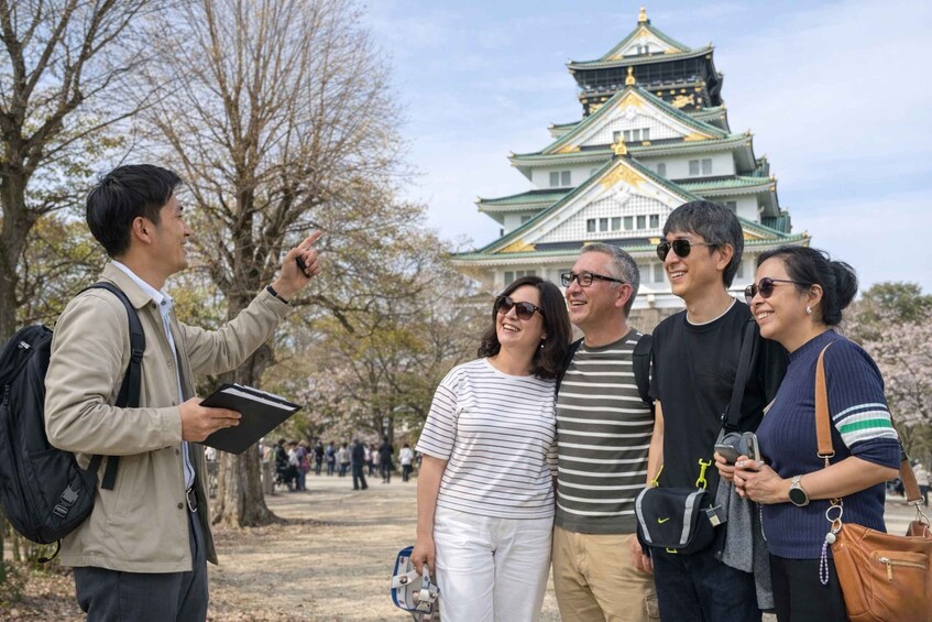 A group of people standing in front of a castle with a green roof and gold accents. 3