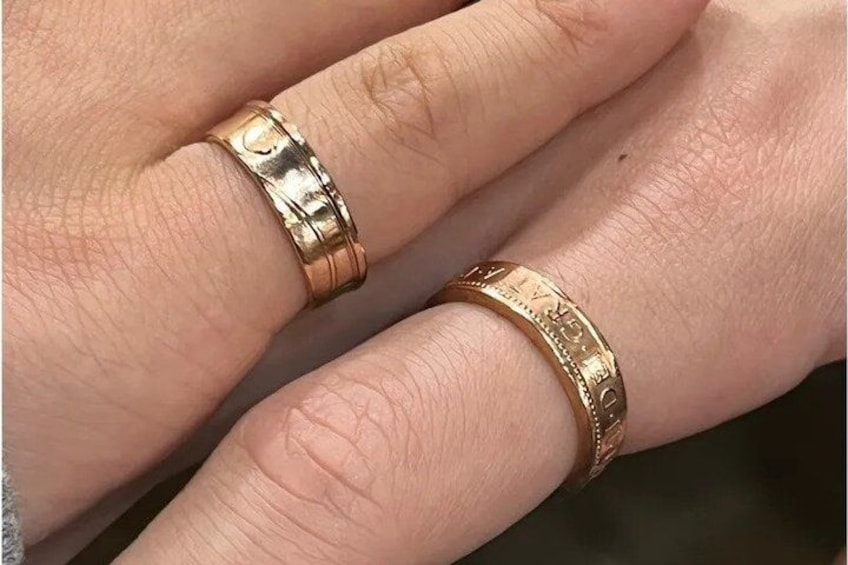 Et nærbillede af en hånd, der bærer en gylden ring med hjerteform og en anden ring med detaljeret indgravering. 2