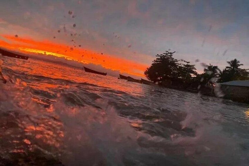 A sunset over a body of water with boats and a shoreline with trees. 2