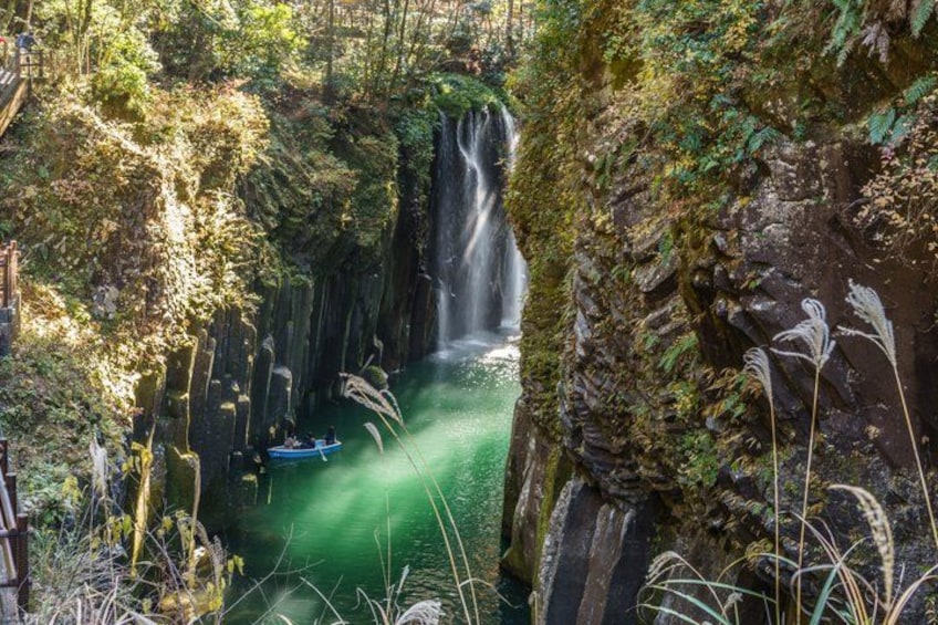 A waterfall in a forested area with a boat on the water. 1