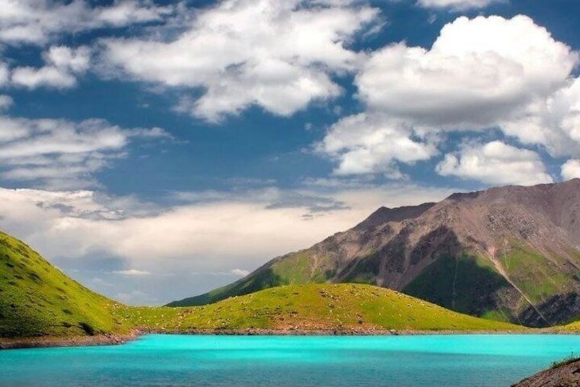 Un lago turquesa rodeado de colinas y montañas verdes bajo un cielo parcialmente nublado. 1