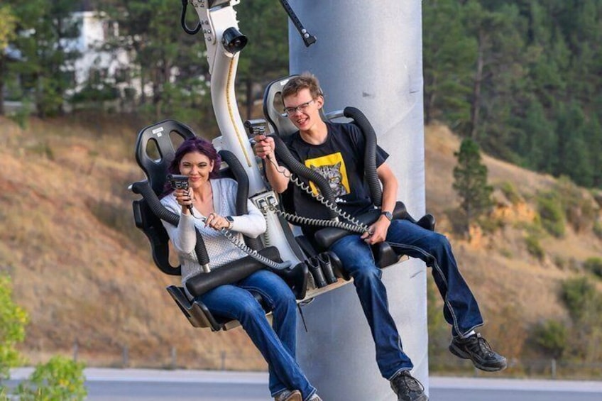 Two people seated on a swing-like structure attached to a large metal pillar, holding phones. 1