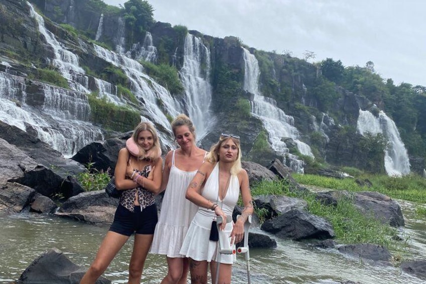 Trois personnes se tiennent près d’une cascade, avec plusieurs chutes d’eau en arrière-plan. 1