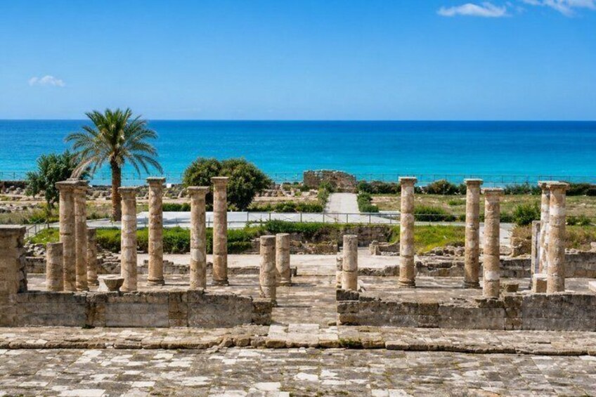 Ancient ruins with columns, palm trees, and a view of the sea. 4