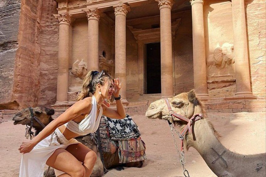 A person sitting on a camel in front of a large ancient stone structure with columns. 2