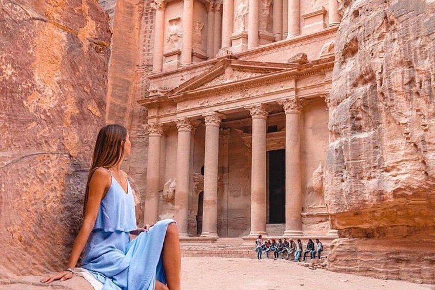 A person sitting in front of a large rock-cut structure with columns and a facade. 5