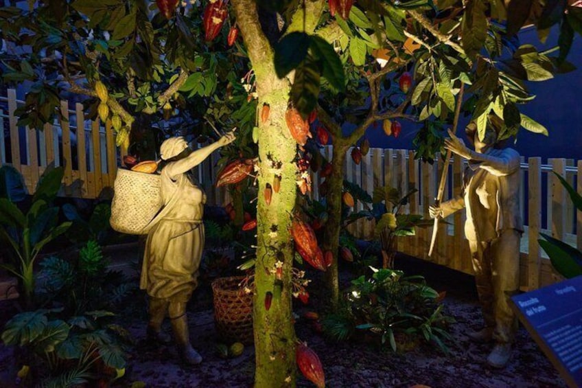 A garden with two statues, one holding a basket and the other holding a tool, surrounded by lush foliage and a wooden fence. 4