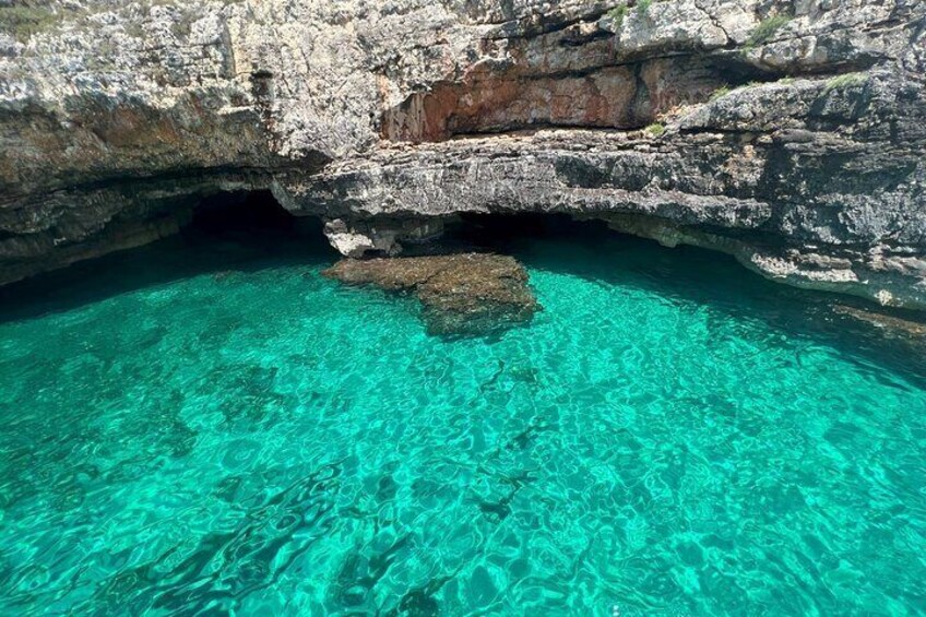 A clear turquoise cave entrance with rocky walls and a visible rock formation in the water. 2