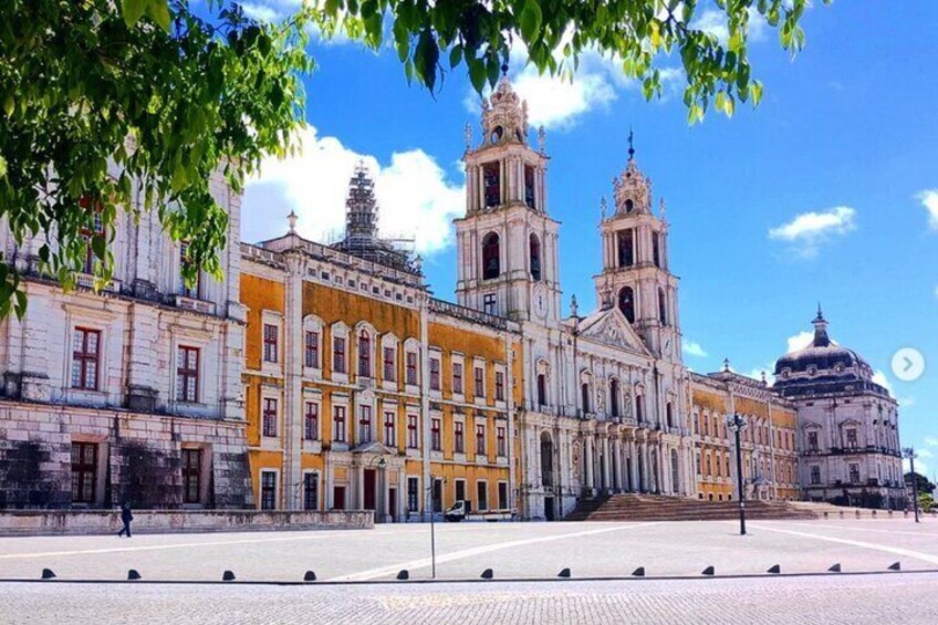 Un edificio histórico con dos torres destacadas y una cúpula, rodeado de una plaza pavimentada. 1