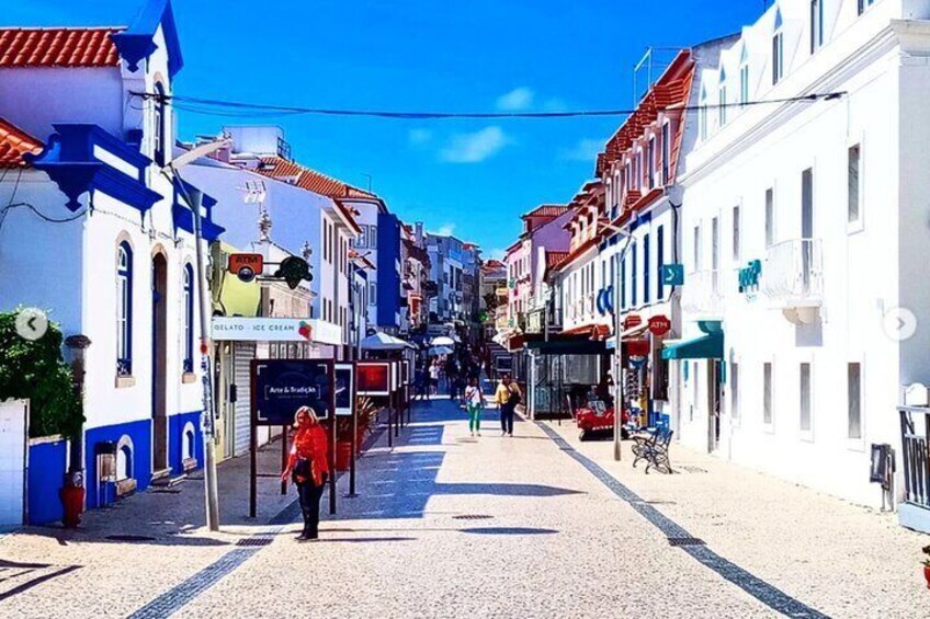 Calle peatonal bordeada de edificios blancos y azules, una heladería y un café. 4