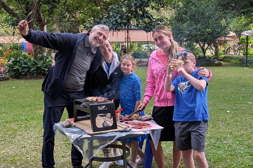 En familj grillar utomhus, och ett bord är dukat med mat och dryck. 5
