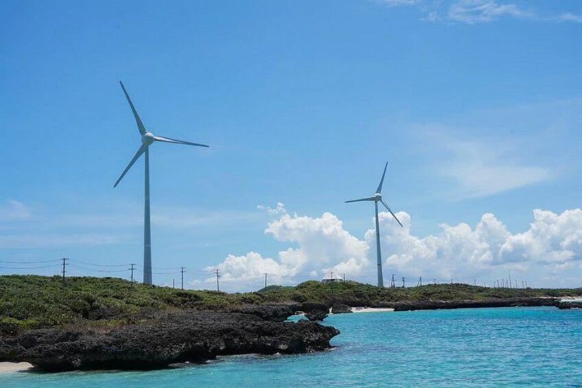Two wind turbines on a coastline with clear skies and calm sea. 5