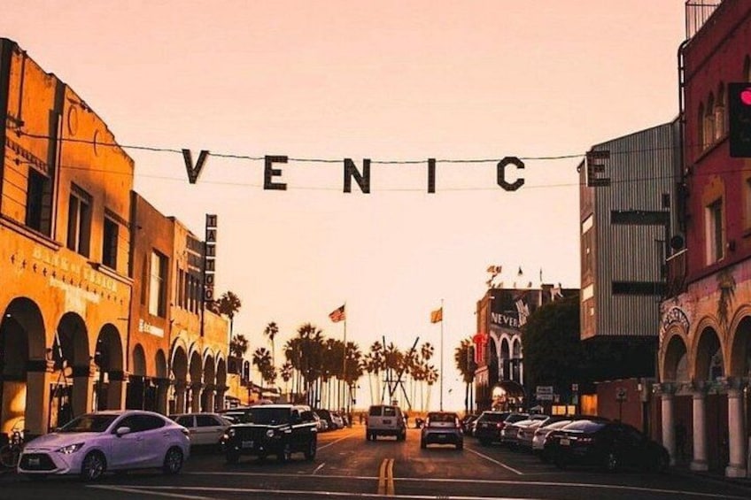 A street with the word 'VENICCI' spelled out in lights, cars parked on the street, and buildings with arches. 1