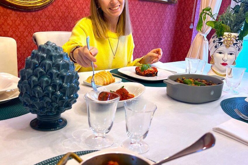 A dining table with a woman eating, a decorative blue vase, and a bowl of food. 2