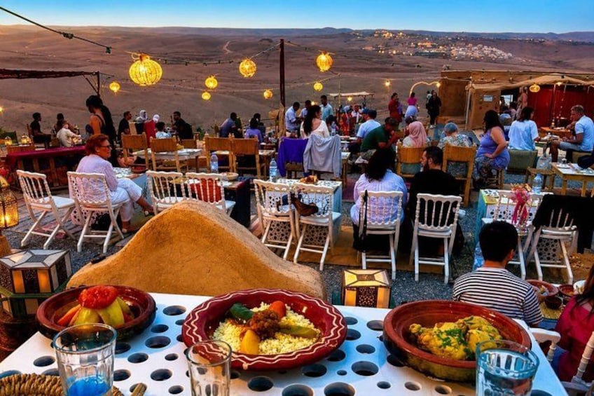 A dining area with tables and chairs, food dishes, and a mountainous landscape in the background. 3