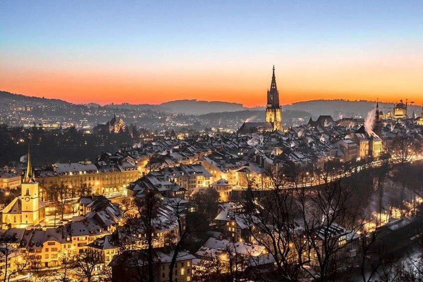 Un paisaje urbano al anochecer con edificios iluminados y una imponente aguja de iglesia. 5