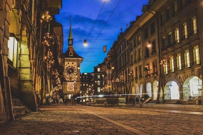 Una calle adoquinada al anochecer con edificios iluminados y una torre del reloj. 3