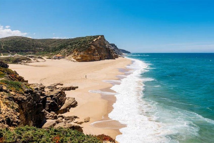 A coastal landscape with a sandy beach, rocky cliffs, and clear blue waters. 5