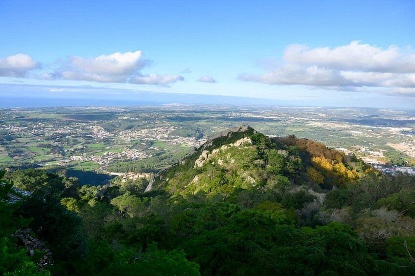 A mountainous landscape with dense forest, a valley with scattered buildings, and a clear sky. 3