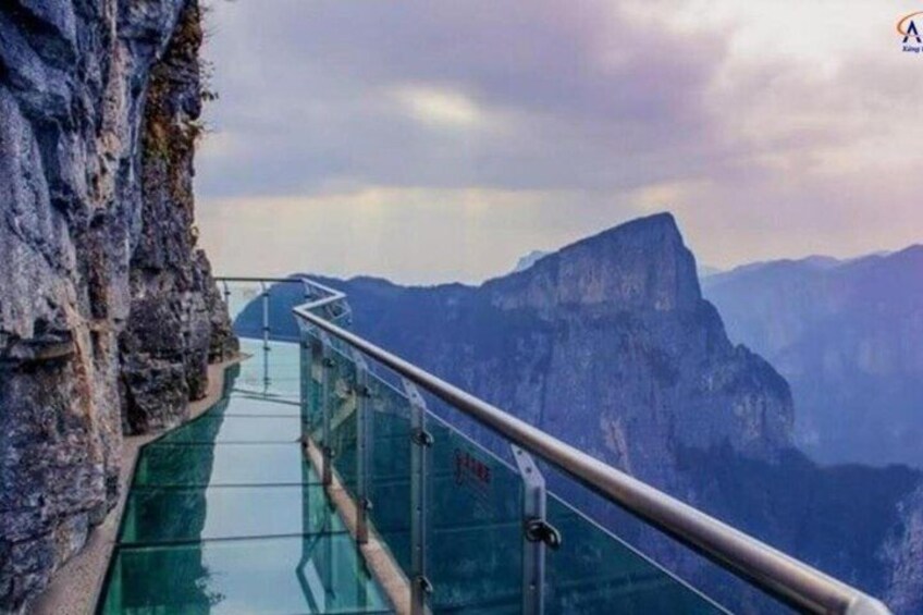 A glass walkway with metal railings overlooking a mountainous landscape. 1