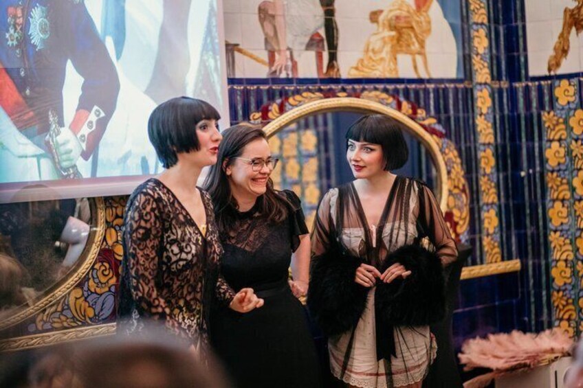Three people in a room with ornate blue and gold decor, including a large mirror and floral patterns. 4